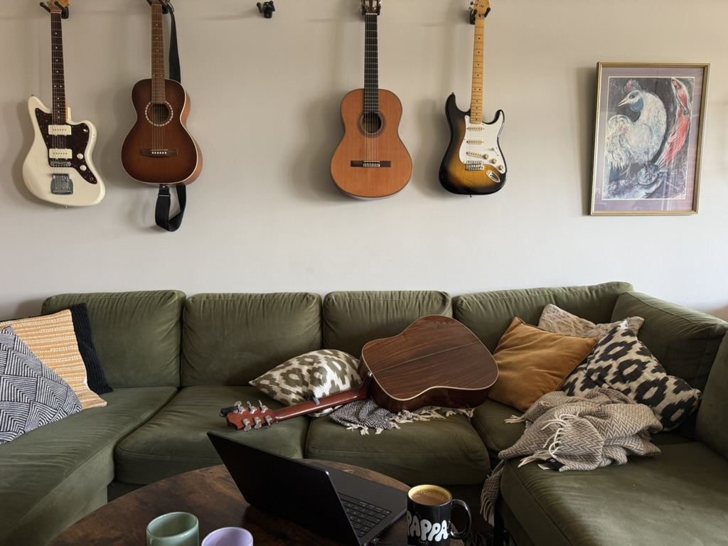 A green sofa beneath four guitars, with an acoustic guitar left on the cushions