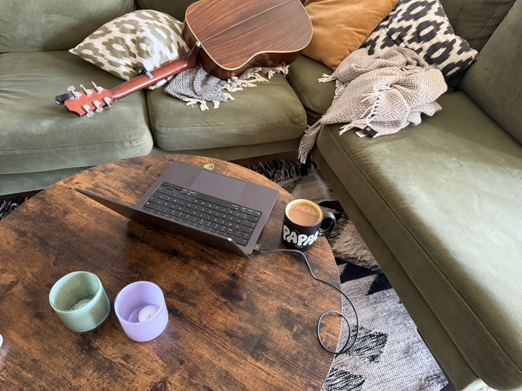 A guitar, laptop and coffee cup arranged around a green sofa