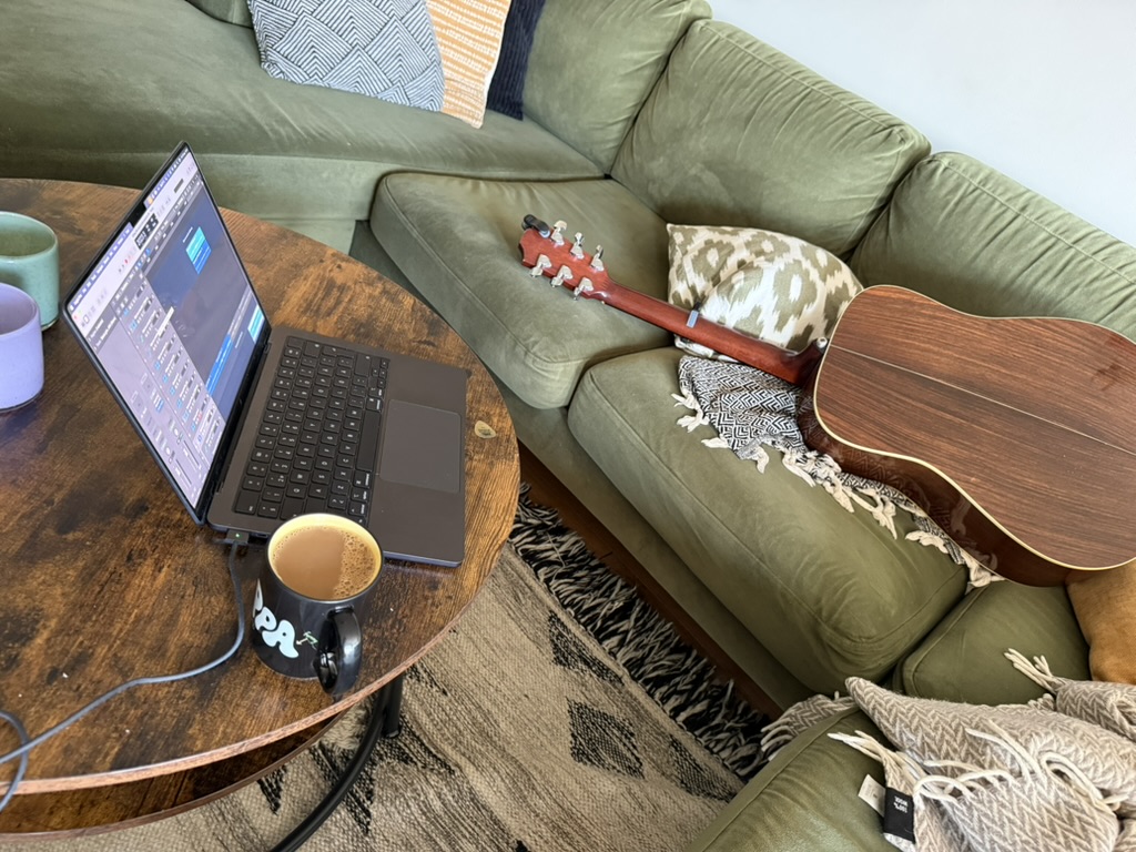 A laptop recording session beside an acoustic guitar on a sofa